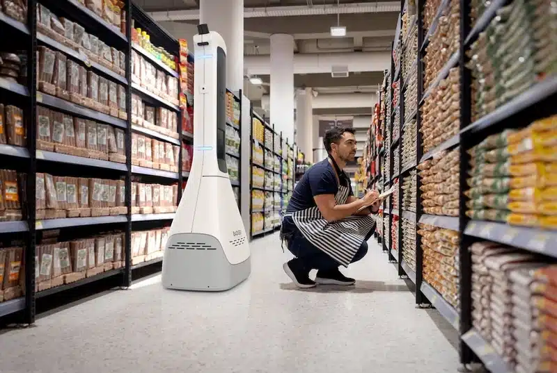 AI retail cobot assisting store worker with shelf inventory in a supermarket aisle
